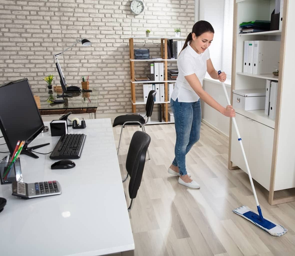 Eine Reinigungskraft führt in einem hellen Büro in München die Bodenreinigung durch, um ein sauberes Arbeitsumfeld zu gewährleisten.