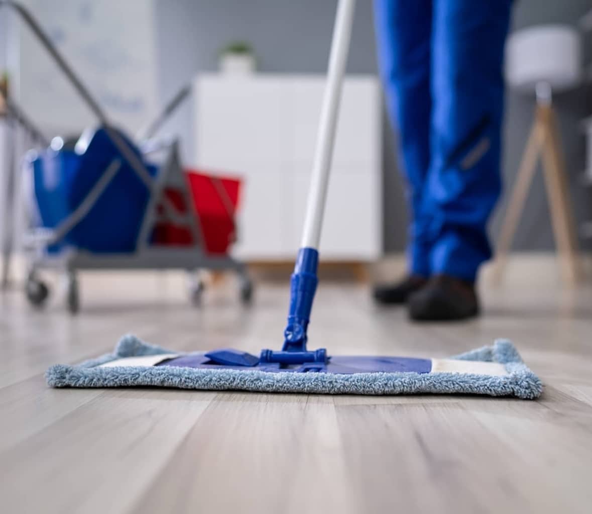 Grundreinigung eines Bodens in München durch eine Reinigungskraft, die einen Mopp verwendet, um den Holzboden zu säubern.