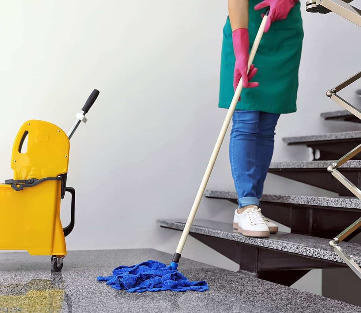 Reinigungsfachkraft bei der Treppenhausreinigung in München, die mit einem Mopp und einem gelben Reinigungswagen arbeitet.