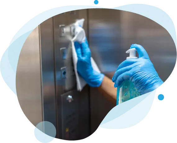 Eine Hand in blauen Schutzhandschuhen reinigt die Knöpfe eines Aufzugs mit einem Sprühdesinfektionsmittel und einem Tuch.