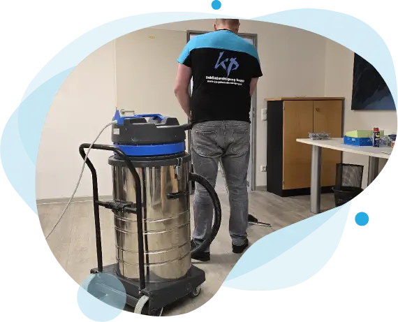 Ein Mitarbeiter der KP Gebäudereinigung GmbH reinigt mit einem professionellen Industriesauger einen Bürofußboden. Auf seinem T-Shirt ist das Firmenlogo gut sichtbar.